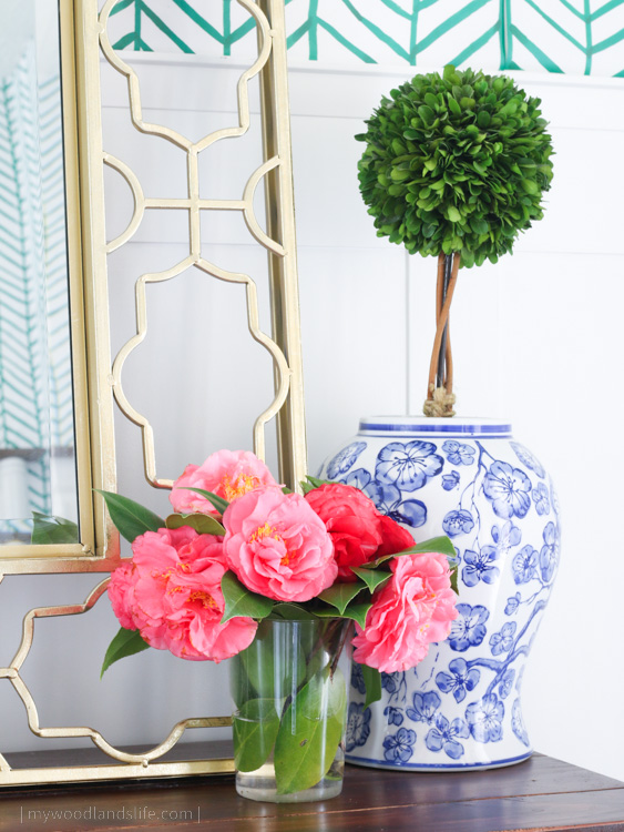 Blue and white vase with topiary and camelia flowers and peel and stick wallpaper in green chevron pattern