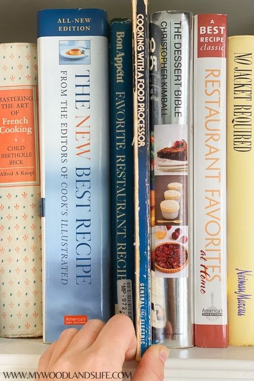 Cookbooks on shelf with hand pulling out Cooking with a Cuisinart