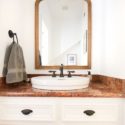 Straight view of powder room sink and countertop with updated wood mirror and modern light fixture