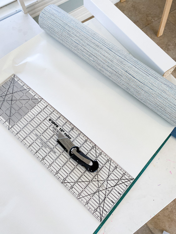 Utility knife and ruler on top of rolled out reusable wallpaper