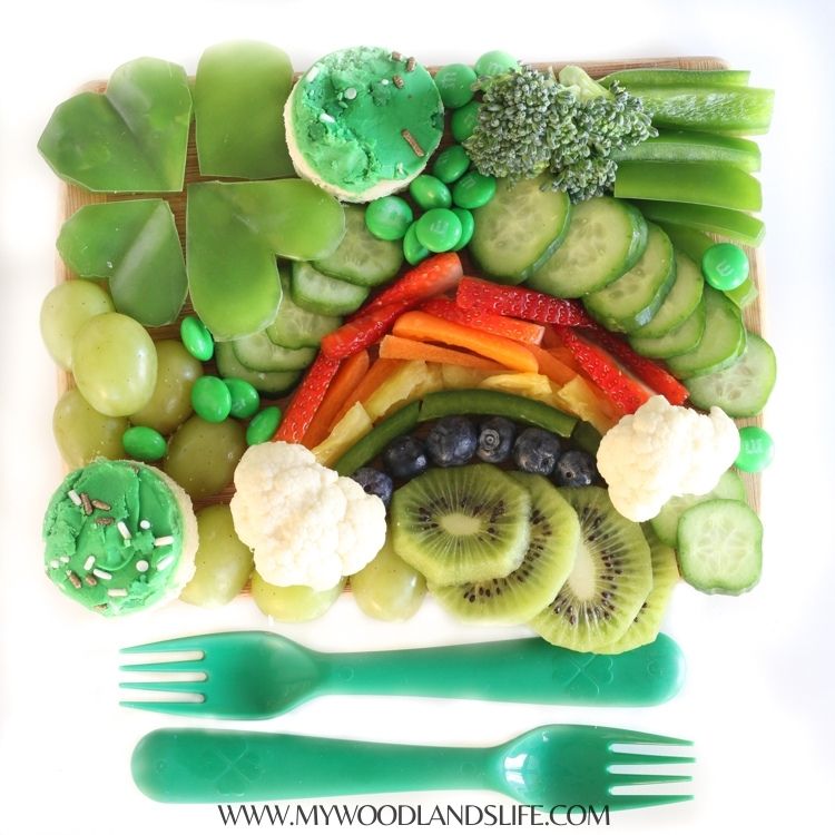 Fruit and vegetables arranged in rainbow and green pattern on wooden cutting board