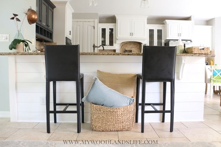Shiplap bar in coastal family room with two black barstools and seagrass basket
