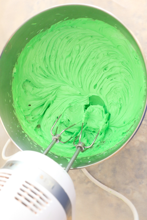 Green icing in metal bowl with electric hand mixer beating the icing